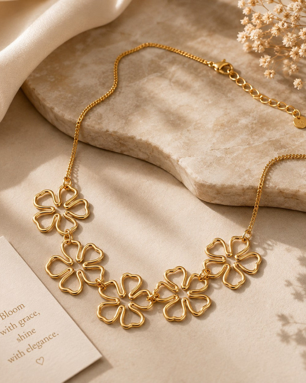Gold-tone five-flower necklace arranged on cream fabric beside a stone tray